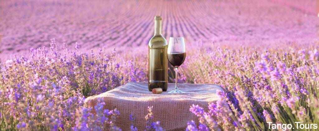 A bottle of wine and glass on a table in front of lavender field.